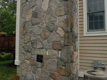 Close-up of exterior stone chimney veneer next to tan siding.
