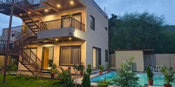 Modern two-story house with outdoor staircase and a lit swimming pool at dusk.