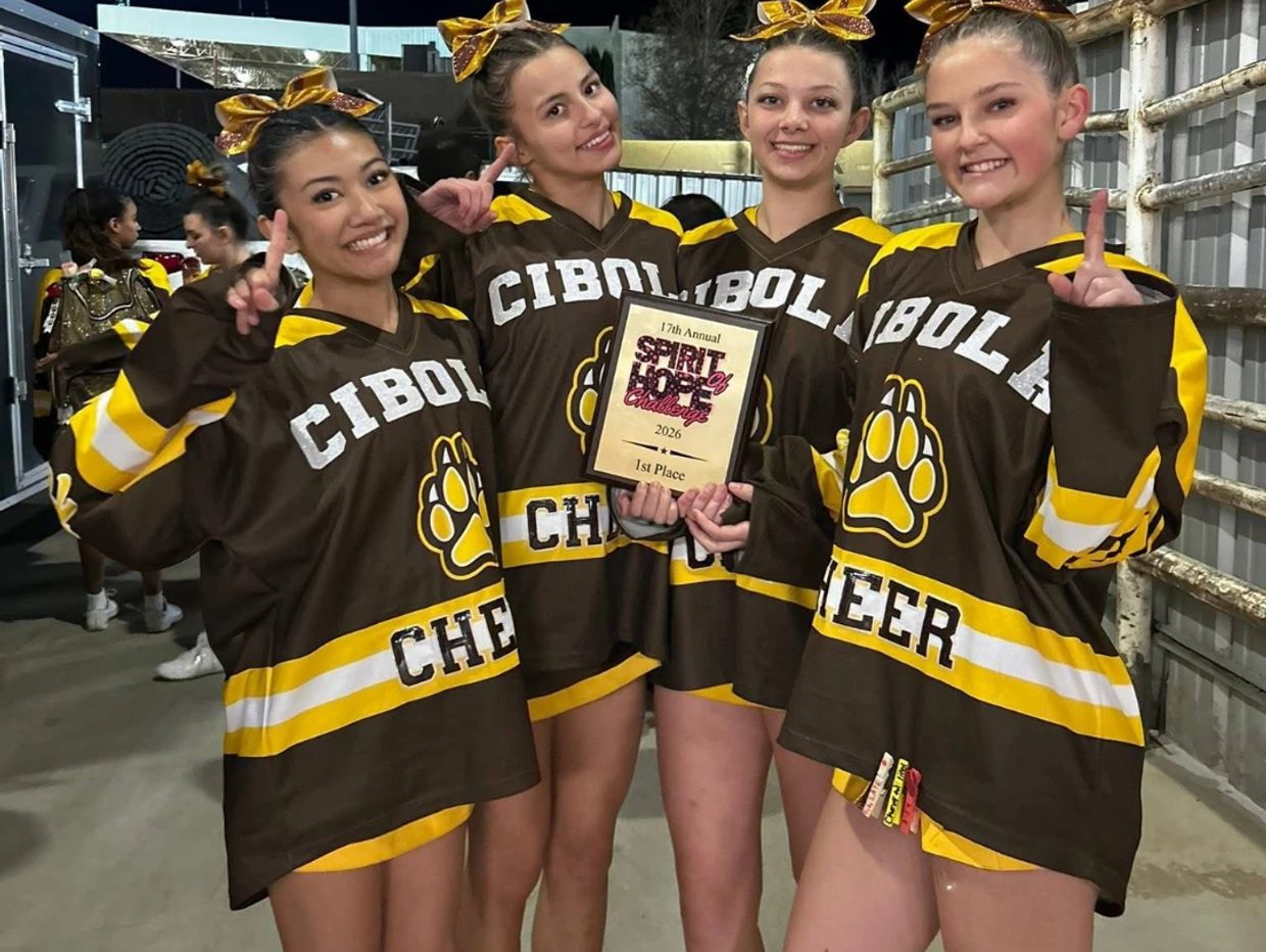 Four cheerleaders from Cibola holding a 1st place award, smiling and showing number one signs.