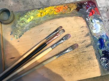 A painter's palette with mixed colors and four paintbrushes.