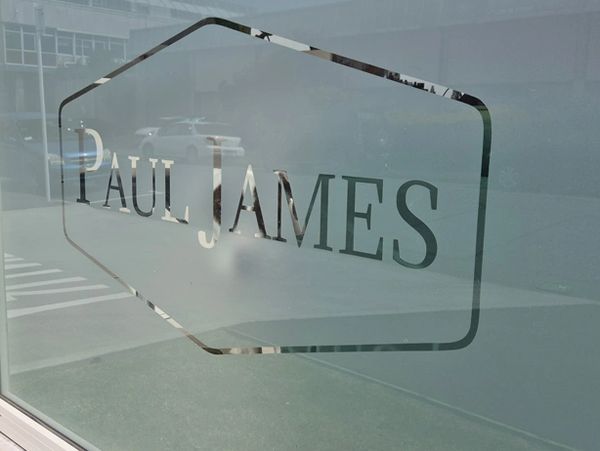 Window decal with 'PAUL JAMES' text on a city street corner.