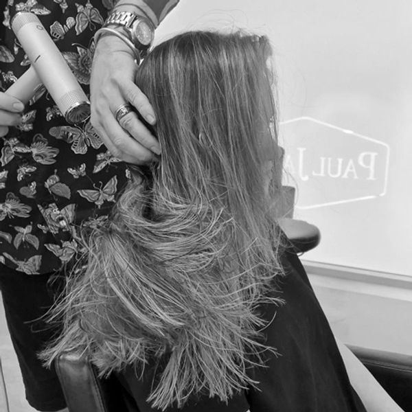 A hairstylist blow-drying a woman's long hair in a salon.