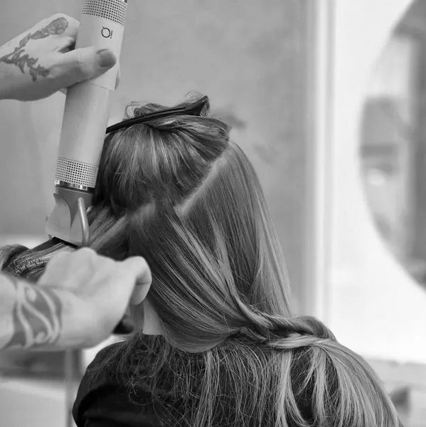 A hairstylist trims a woman's hair with clippers, sectioning it with a clip.