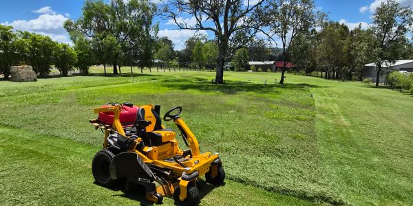 Yellow lawn mower cutting grass on a sunny day in a large green yard.