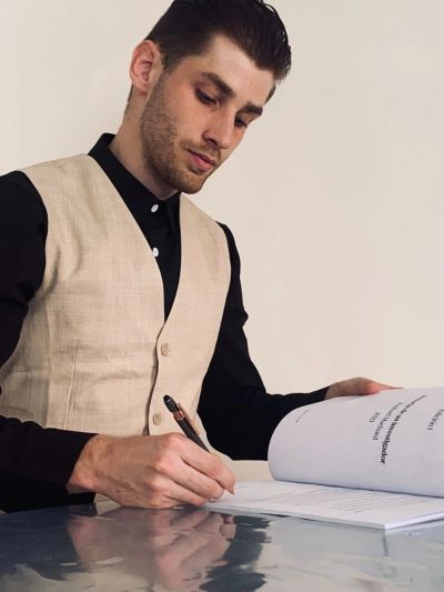 A man in a beige vest and black shirt signing a document.