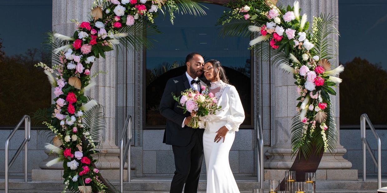 A couple poses together under a floral arch.