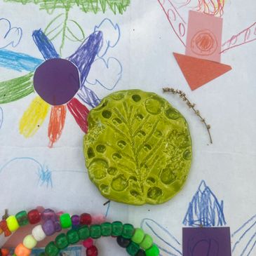 Colorful kids' artwork with clay and beads on paper.