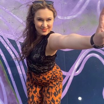 Woman posing confidently in front of purple graffiti wall.