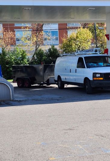 White van with attached trailer at a gas station.