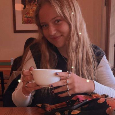 Young woman smiling while holding a white cup in a cozy café.