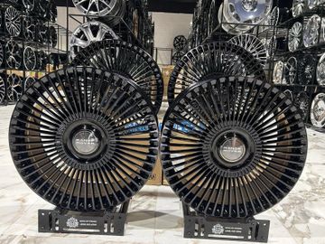 Two black radial fans displayed in a showroom filled with car rims.