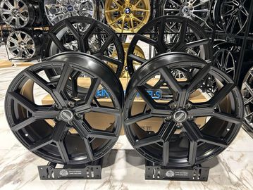 Two black alloy wheels displayed on a marble floor with various wheels in the background.