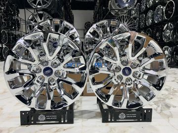 Two shiny chrome Ford wheel rims displayed on stands.