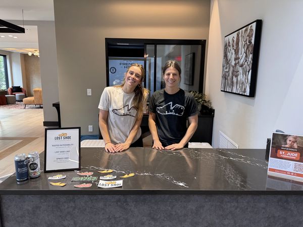 Two employees at a table with Lost Shoe beer cans and stickers at an off-site event.