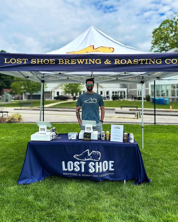 Employee at Lost Shoe branded tent with beer cans and POS system at off-site event.