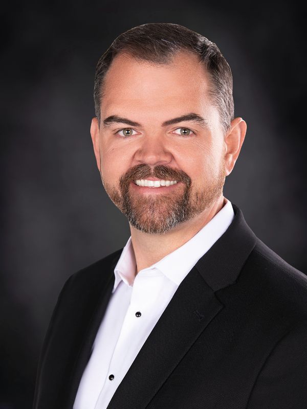 Professional man in suit smiling against a dark background.