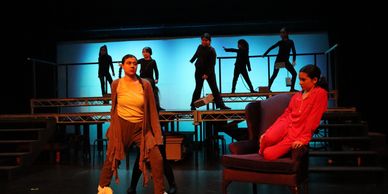Actors performing a dramatic scene on stage with blue backlighting.