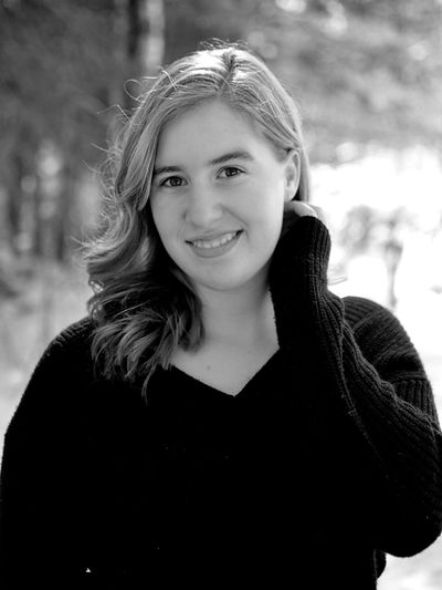 Young woman smiling gently outdoors in black and white portrait.