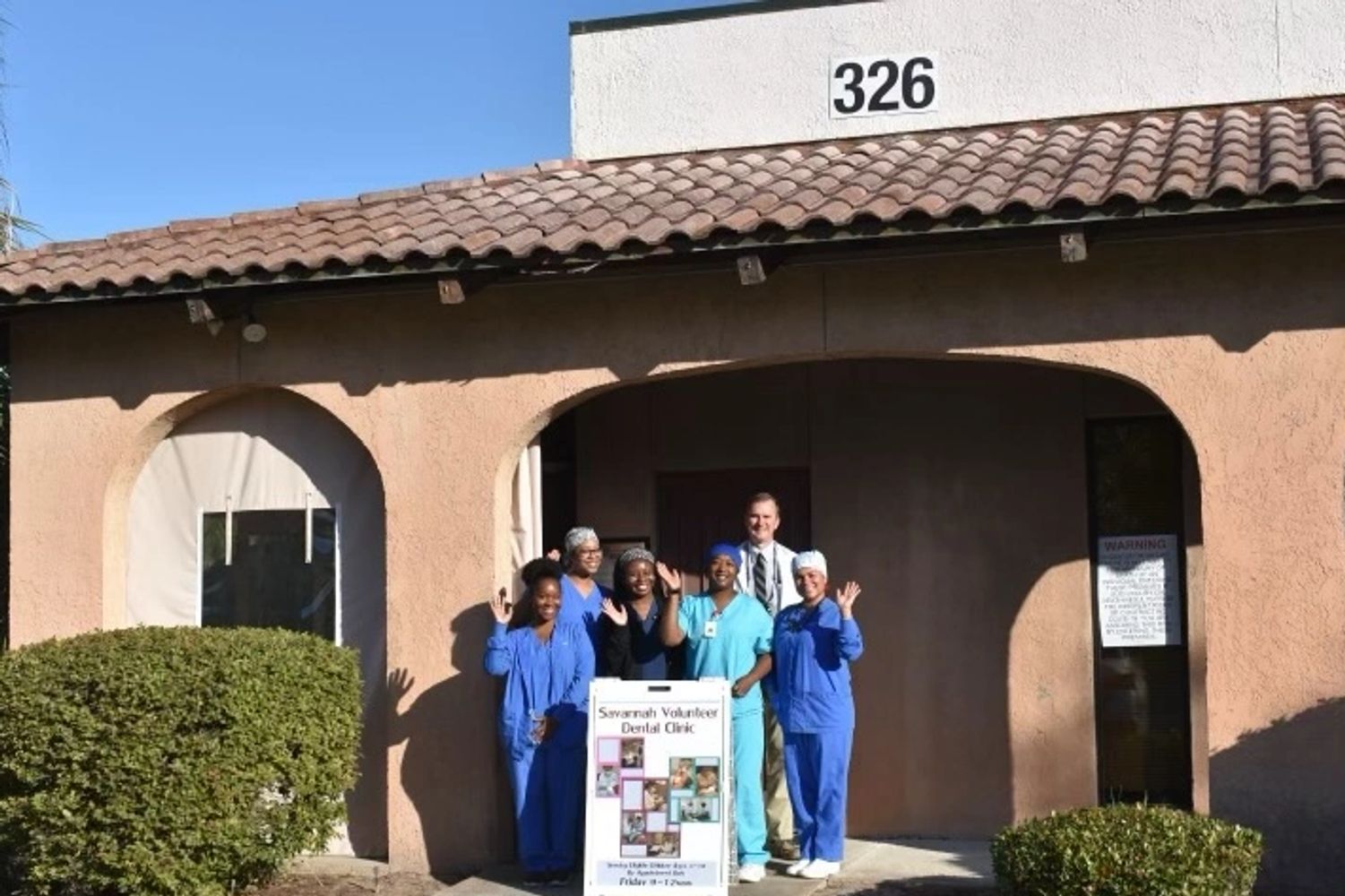 group of dental office workers standing in front of office with a sign for the clinic