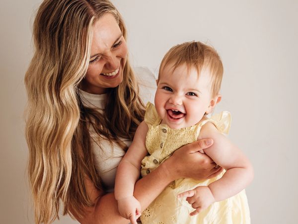 A joyful mother holding her laughing baby girl in a yellow dress.