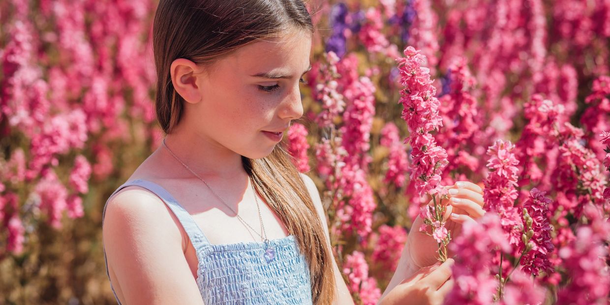 Girl admiring pink flowers in a sunny garden.