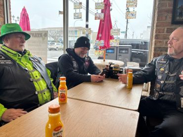 Three men sitting at a table with orange juice bottles.