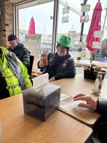 Man in green hat holding a cup at a cafe table.
