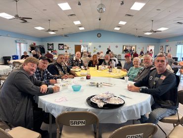 Group of people gathered around a table enjoying a meal in a community hall.