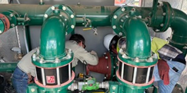 Workers inspect large green industrial pipes.