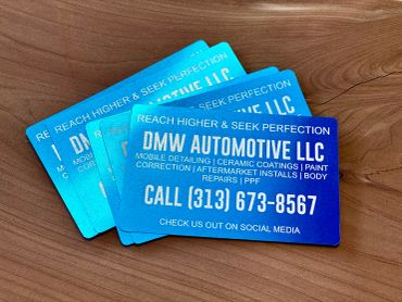 Blue business cards for DMW Automotive LLC on a wooden surface.