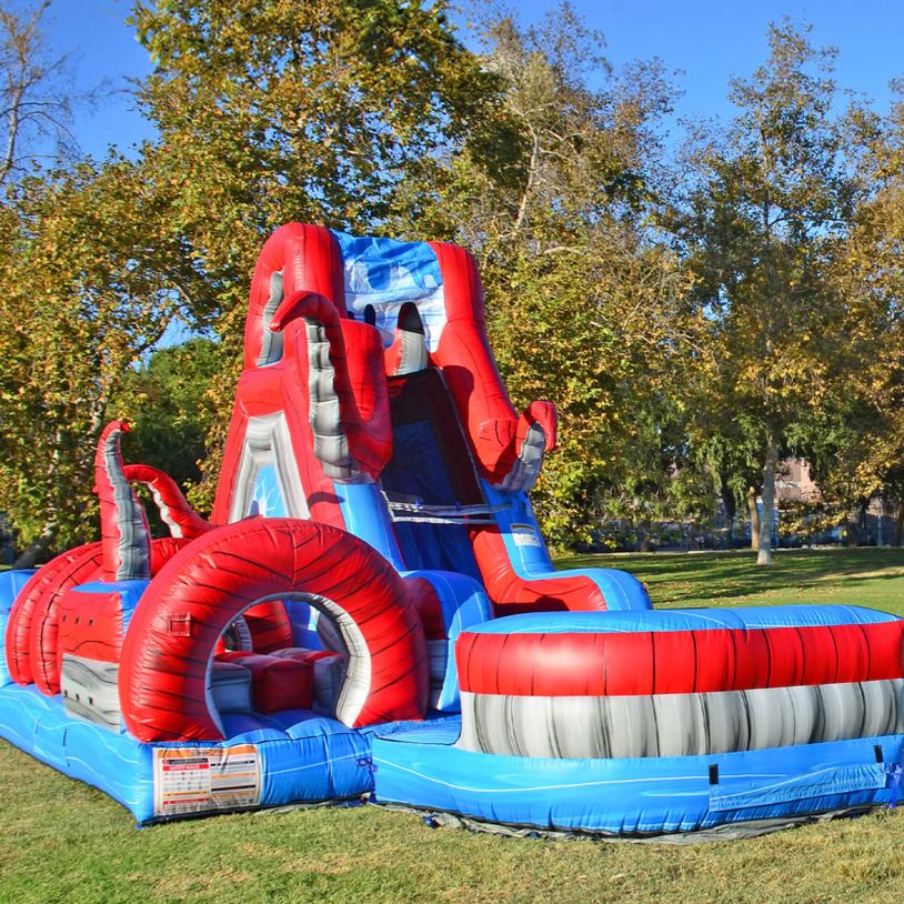 Colorful inflatable water slide set up in a grassy park area on a sunny day.