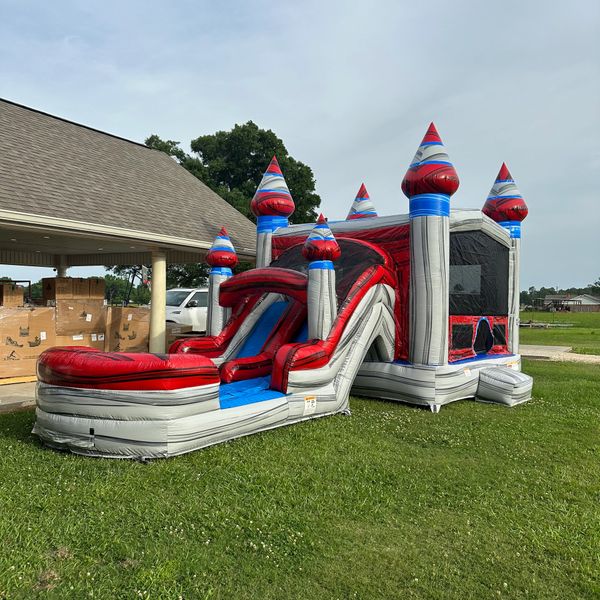 A red, white, and blue inflatable bounce house with a slide on a grassy lawn.