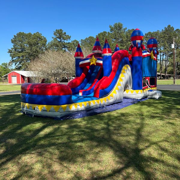 Colorful inflatable bounce house and slide set up on green grass under a clear blue sky.