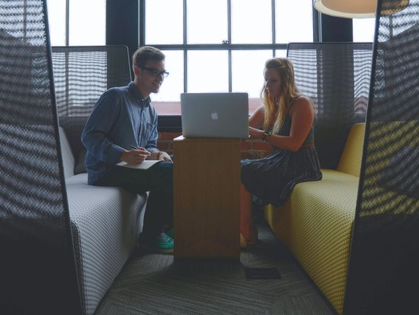 Two people collaborating on a laptop in a modern office lounge.