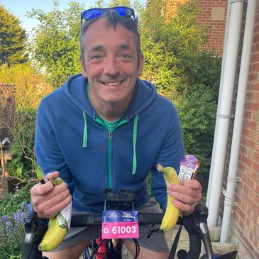 Smiling cyclist holding bananas and energy bars, ready for a ride with helmet in hand.