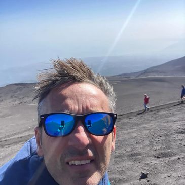Man with blue reflective sunglasses taking a selfie on a barren mountain landscape.