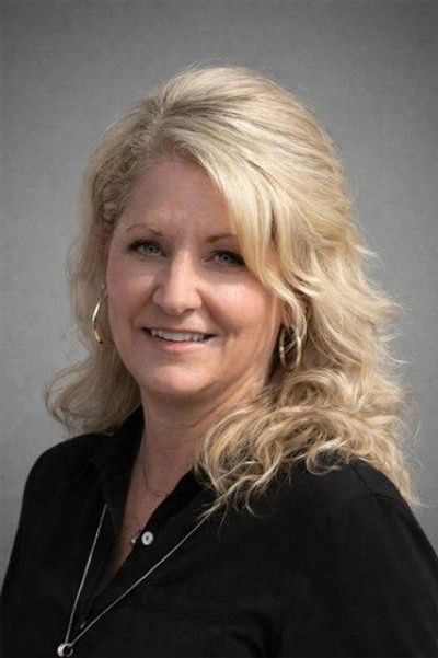 Portrait of a smiling blonde woman with curly hair wearing a black top.