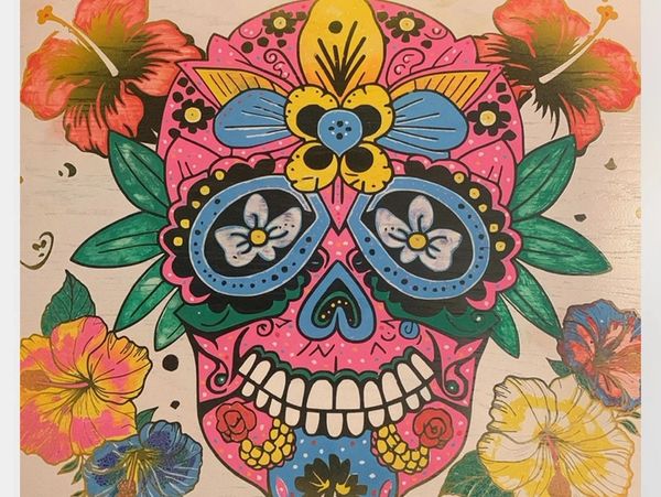 Colorful sugar skull surrounded by vibrant flowers.