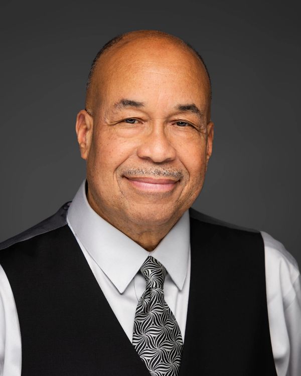 Smiling man in formal attire with patterned tie and black vest.