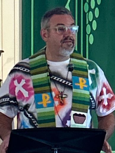 A man wearing colorful religious attire speaks at a church podium.