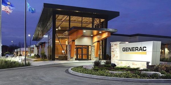 Modern Generac building at dusk with illuminated sign and flags.