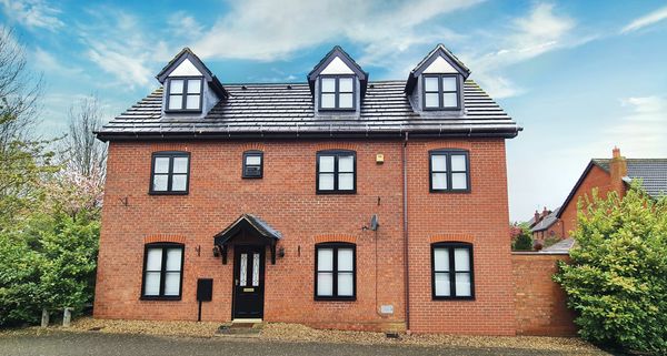 A large red brick house with black-trimmed windows and a black front door under a blue sky.