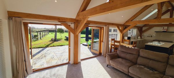 Cozy living space with wooden beams and large open doors to a sunny garden.