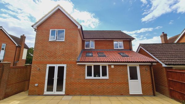 Modern brick house with tiled roof and multiple windows under a blue sky.