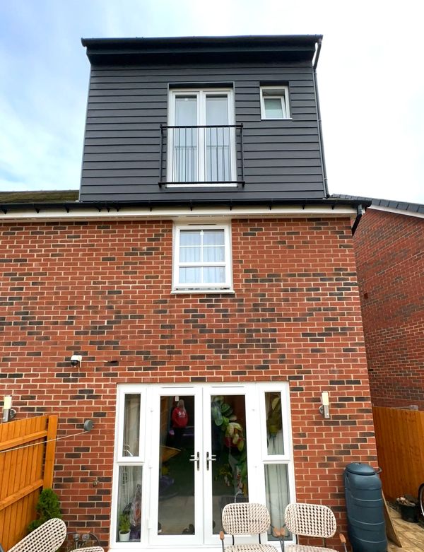 A modern three-story brick house with a balcony and patio seating.