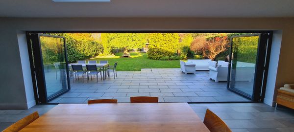 Open patio doors reveal a spacious garden with outdoor seating and lush greenery.