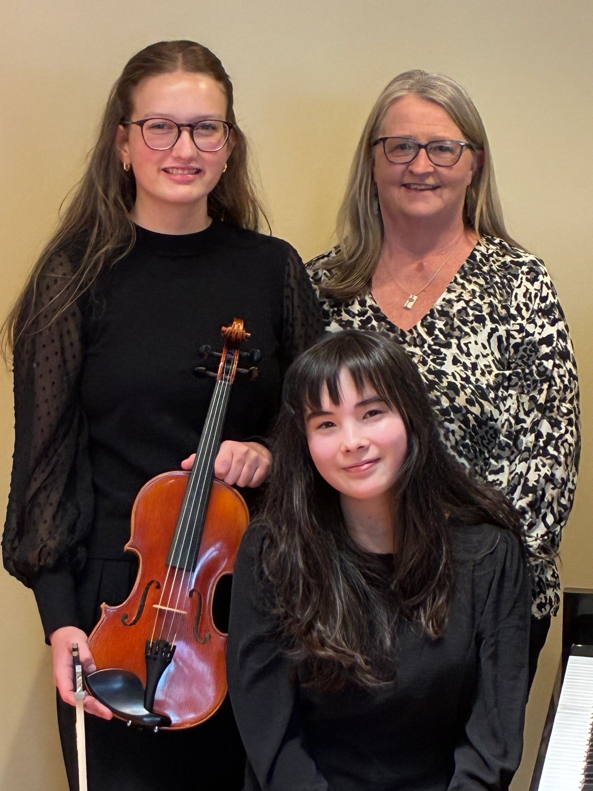 Three women posing, one holding a violin and bow, smiling warmly.