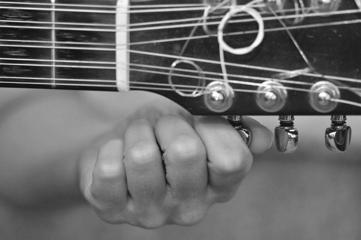 Close-up of a hand tuning guitar strings on the headstock.