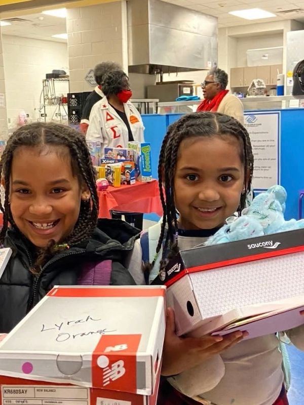 Two smiling girls holding shoe boxes indoors.