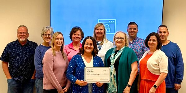Group of ten people posing with a large check in an indoor setting.